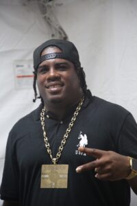 Asa Bantan smiling in a black cap and his Bouyon Boss chain